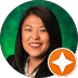 Professional woman with straight dark hair, smiling, wearing a dark blazer and white top, posed in front of a green background. An orange location marker icon with a white star hints at her expertise as a chiropractor in Denton, Texas.