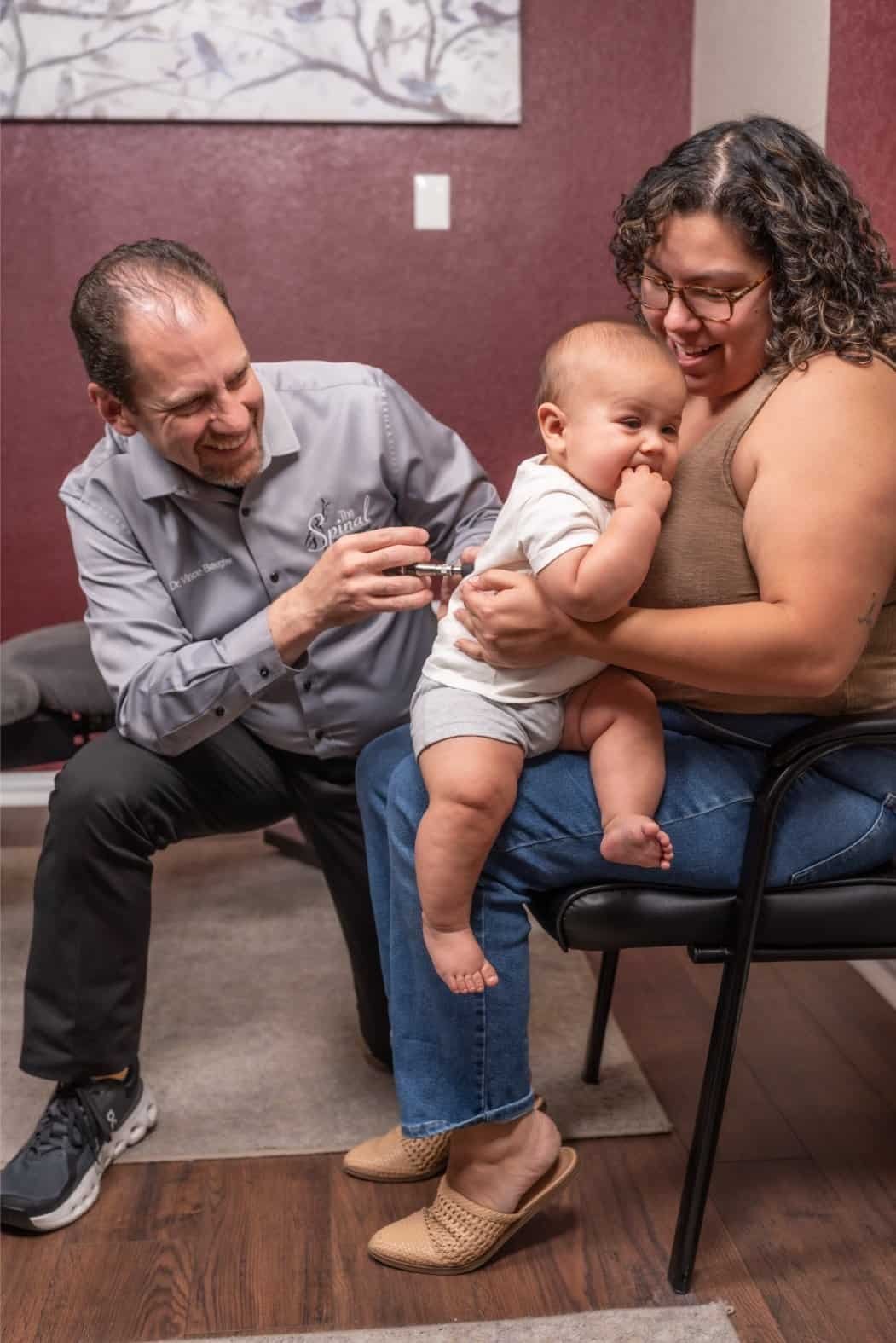 A smiling healthcare provider gives a vaccine to a baby sitting on their mother’s lap in a clinic. The calm scene reflects the caring touch you’d expect from a trusted chiropractor in Denton, Texas.